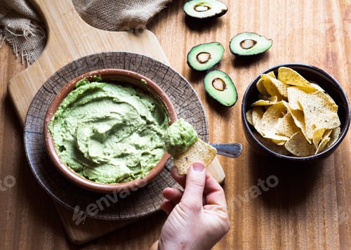 Preview: Man hands eating a bowl of nachos with guacamole on a yellow background. Concept: Mexican food
