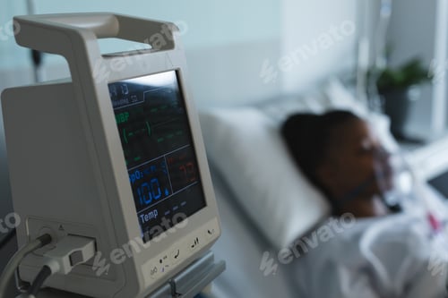 Preview: Patient monitoring device next to african american female patient lying on bed in hospital room