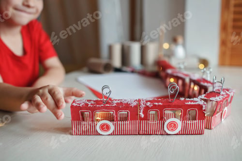 Preview: Boy plays with crafted advent calendar like train or cable car made with toilet paper rolls at home