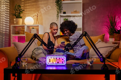 Preview: Two diverse women using phone and recording internet podcast in a studio
