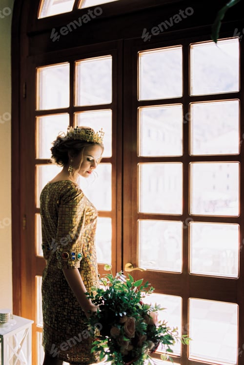 Preview: Bride in the crown stands near the door and looks at the bouquet