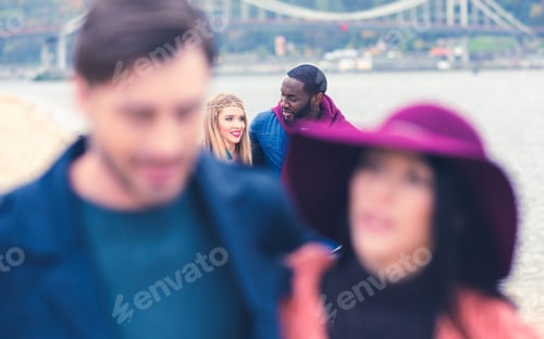 Preview: Young people having pleasant stroll on river beach. Blurred couple on foreground