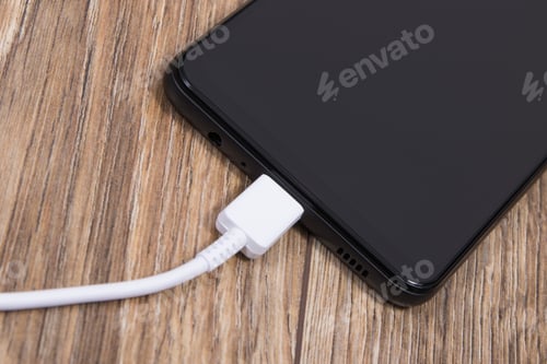 Preview: Black smartphone and connected white cable of charger. Telephone charging