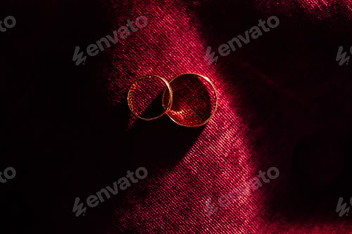Preview: Close-up of wedding rings on a red background in a ray of sun.