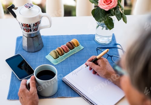 Preview: Hands of a senior woman holding a vintage pen and writing on a paper sheet. Coffee time outdoor