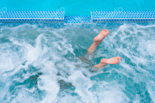 Preview: Overhead view of diving boy's feet in splashing outdoor swimming pool