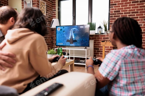 Preview: Multiethnic friends sitting at home in living room while playing space videogame simulator together.