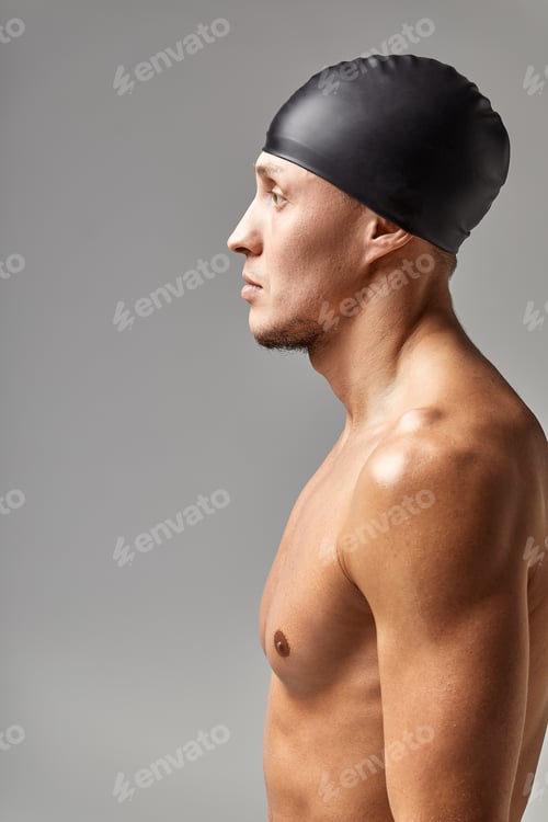 Preview: portrait of a young man swimmer wearing a rubber hat, standing against a gray background hat getting