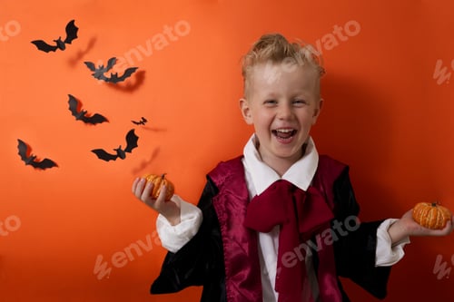 Preview: A boy in a vampire costume laughs and holds a halloween pumpkin on an orange background