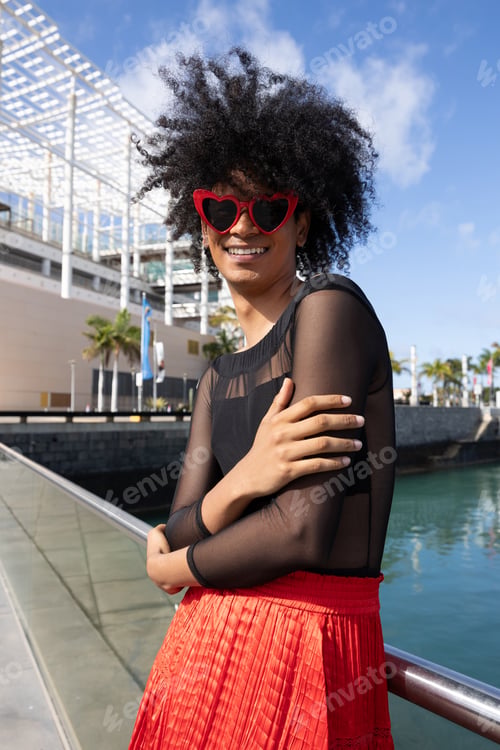 Preview: portrait of smiling queer person with afro hair and red heart glasses looking at the camera