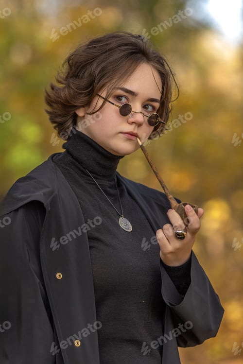 Preview: a young woman in strict black clothes and a top hat on her head, vintage glasses in an autumn park