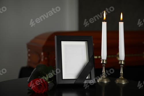 Preview: Black photo frame with burning candles and red rose on table in funeral home