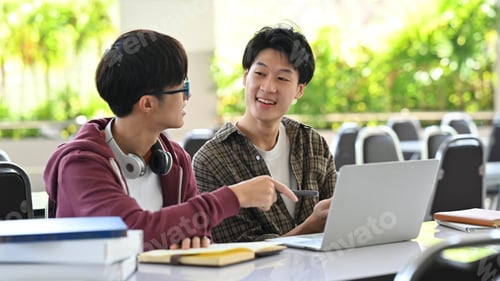 Preview: University students using laptop, working together on academic project.