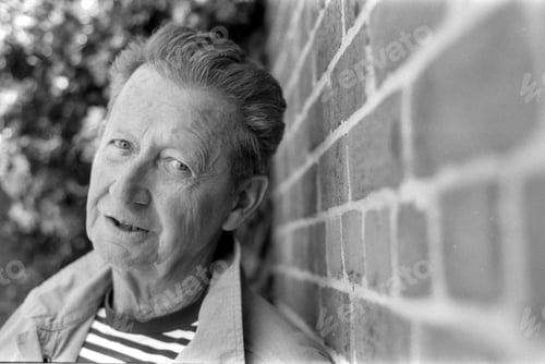 Preview: Senior man leaning against brick wall in grainy monochrome analog photo