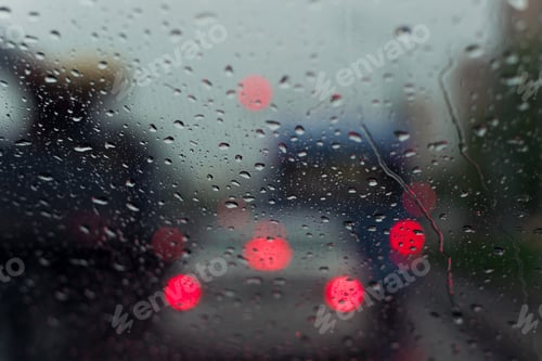 Preview: Raindrops on the glass of the car. Blurred lights of a city traffic jam in the evening. Wet surface