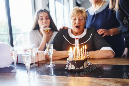 Preview: Blowing the candles. Senior woman with family and friends celebrating a birthday indoors