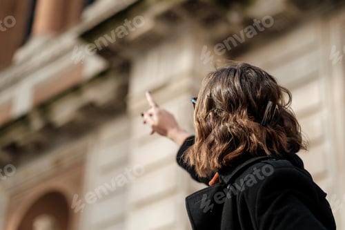 Preview: Unrecognizable tourist woman pointing at an historical building.