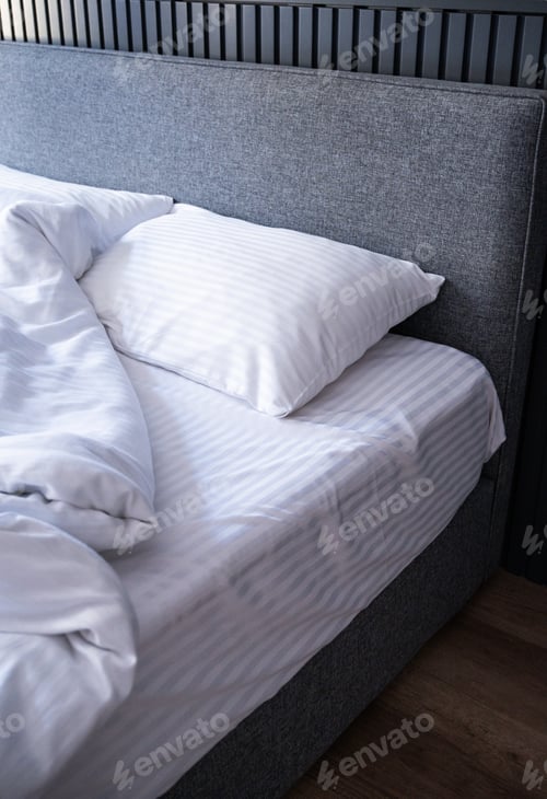 Preview: Modern grey bed with white striped bedding in natural light setting.
