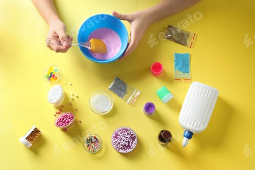 Preview: Little girl making slime toy on yellow background, top view