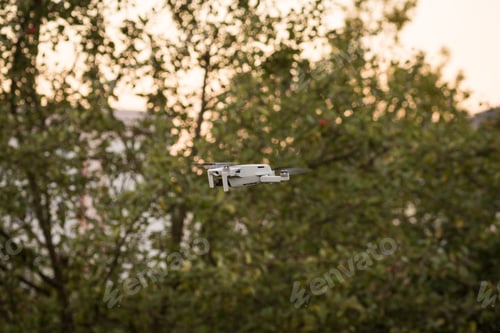 Preview: Bright summer day outdoors with a small drone flying in the air surrounded by greenery