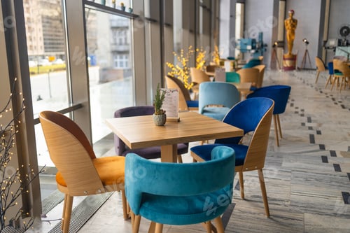 Preview: Modern white cafe interior with color tables with chairs standing next to them. Large windows and an
