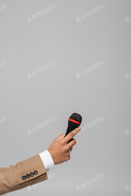 Preview: Cropped view of hand of event host in brown jacket holding wireless microphone during performance