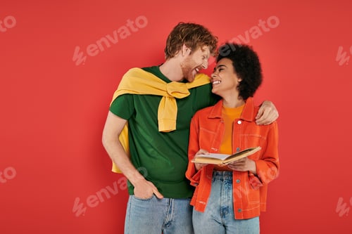 Preview: interracial couple hugging and reading book on coral background, cultural diversity, vibrant colors,