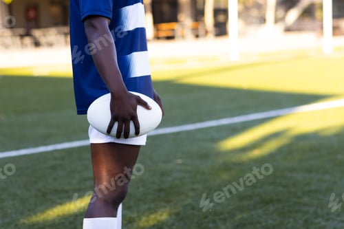 Preview: African American young male athlete holding rugby ball, wearing blue and white, copy space