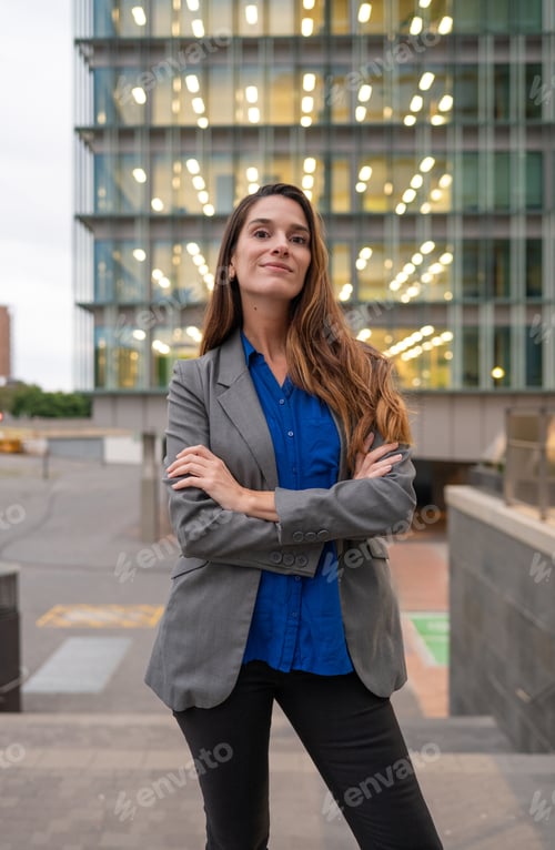 Preview: Confident businesswoman smiling with arms crossed in front of modern building
