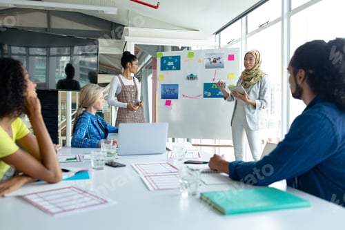 Preview: Mixed-race businesswoman in hijab giving presentation on flip chart during meeting