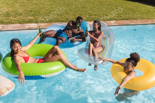 Preview: Diverse group of friends having fun playing on inflatables in swimming pool