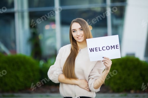Preview: Businesswoman with long Hair Holding a sign Board with a Welcome has Airport Background