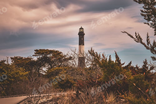 Preview: View of the Fire Island lighthouse in Long Island under a stormy sky with bushes around it.