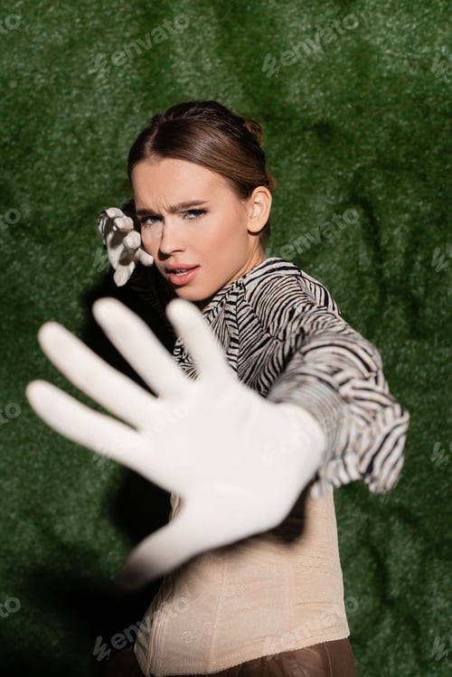 Preview: young trendy model in blouse with zebra print and gloves showing no gesture near grassy background