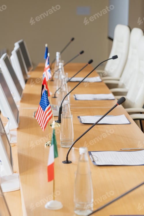 Preview: Row of bottle with water, national flags, microphones, computer monitors and papers