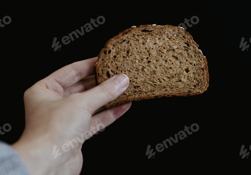 Preview: A woman's hand holds a piece of bread with sunflower seeds.