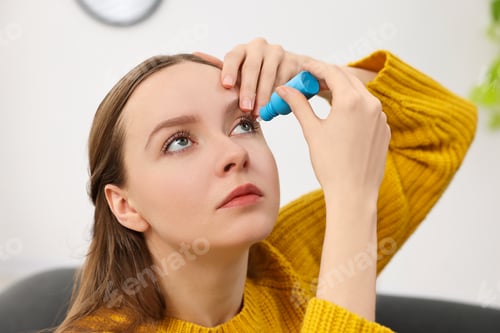 Preview: Young woman applying medical eye drops indoors, closeup