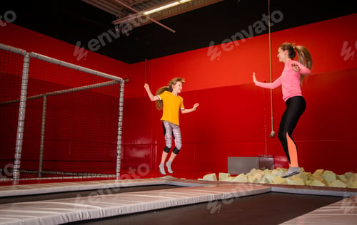 Preview: Happy mother and daughter jumping on trampoline in fintess center