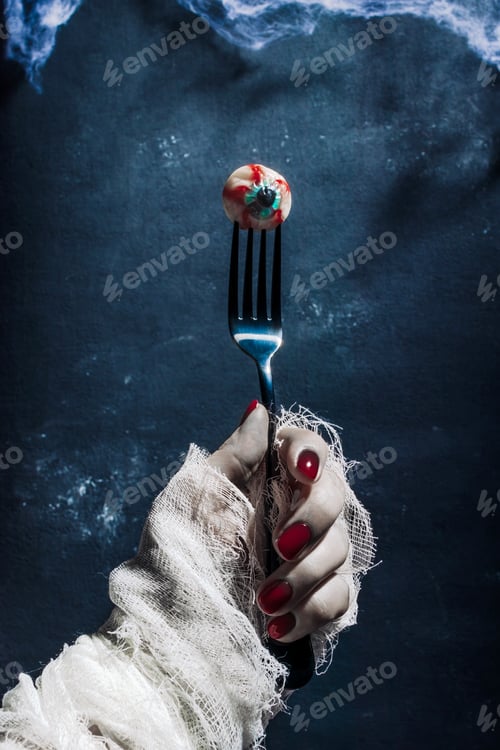 Preview: A bandaged zombie hand holds an eye impaled on a fork