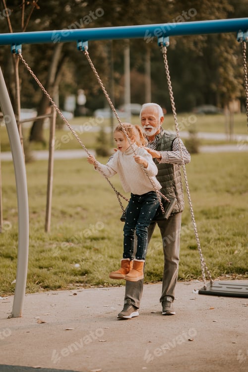 Preview: Grandfather spending time with his granddaughter in park playground on autumn day