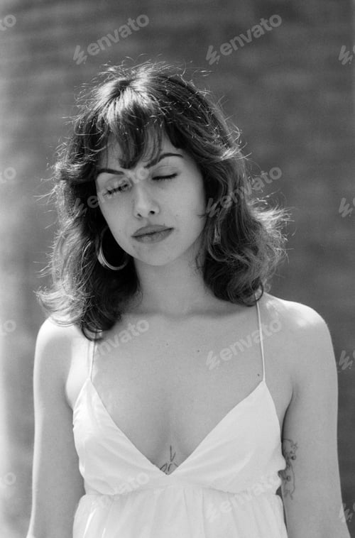 Preview: Relaxed B&W portrait of young woman with eyes closed outdoors.