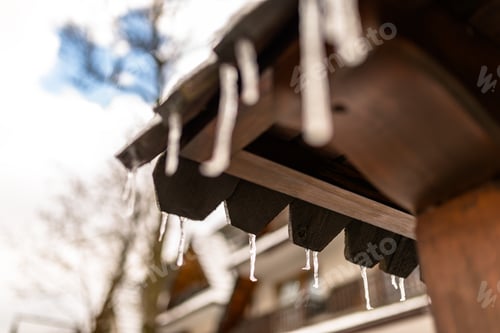 Preview: Hanging icicles from the roof of a wooden building on a winter frosty day, a lot of snow on the roof