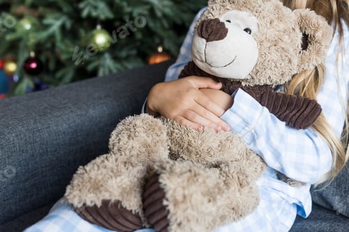 Preview: cropped shot of child hugging teddy bear and sitting on couch at christmas time
