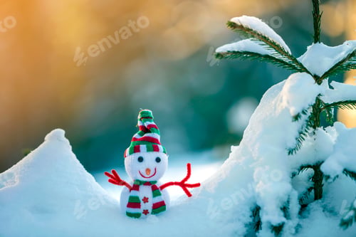 Preview: Small funny toy baby snowman in knitted hat and scarf in deep snow outdoors on bright blue and white