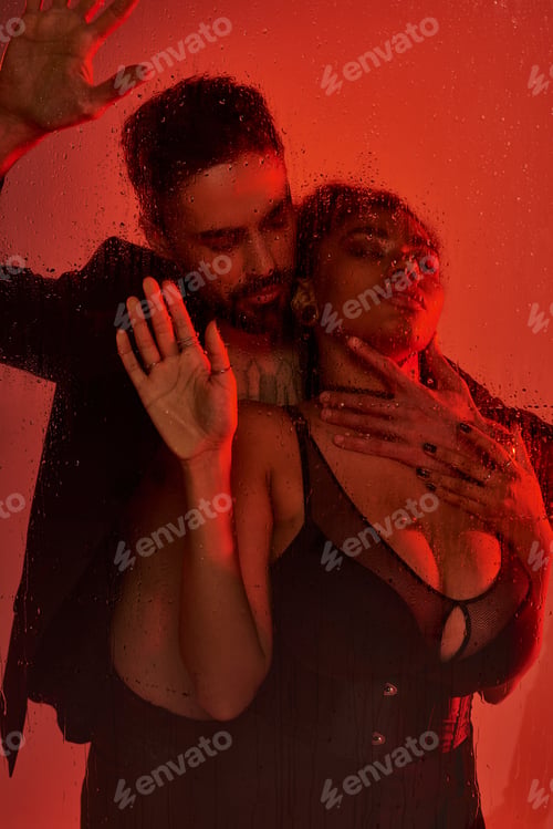 Preview: Passionate embrace of a couple behind misted glass in a warm red lit atmosphere