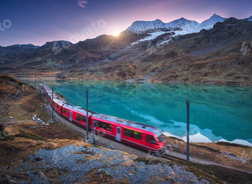 Preview: Moving modern red train near azure mountain Bianco lake, snowy rocks and colorful purple sky