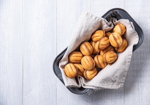 Preview: handmade nuts baked with caramel in a baking dish on a white table.