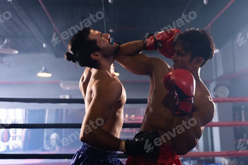 Preview: Sportsman muay thai boxer training fighting in gloves in boxing cage at the gym.