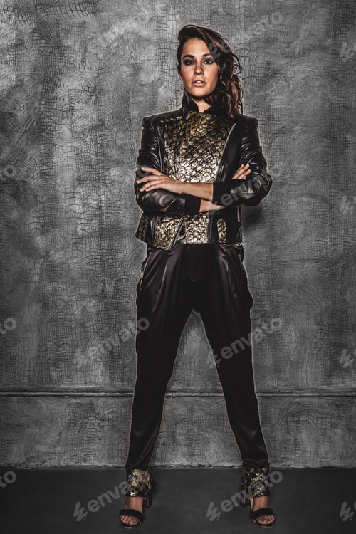 Preview: A female model dressed in black poses in front of a textured gray wall.