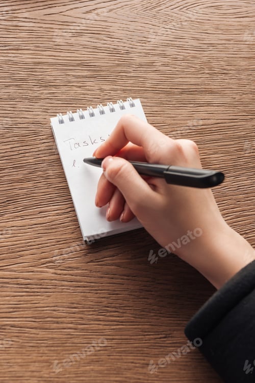 Preview: Cropped view of woman writing in notebook on wooden surface